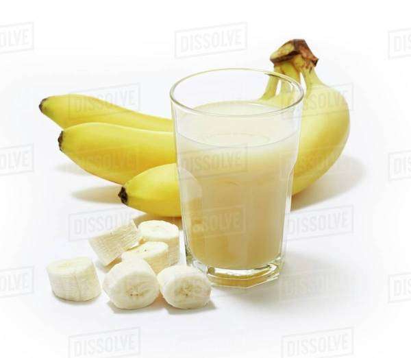 A glass of banana juice with bananas in the background and banana slices next to it Stock