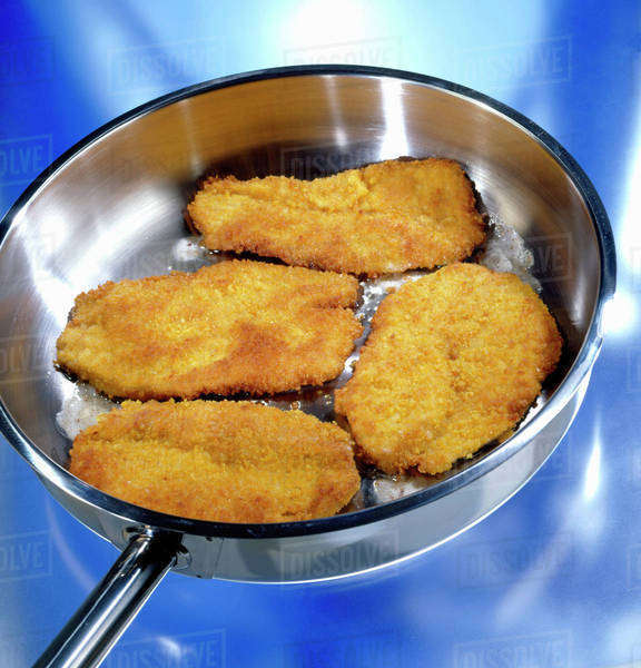 Four breaded pork escalopes being fried in a frying pan Stock Photo