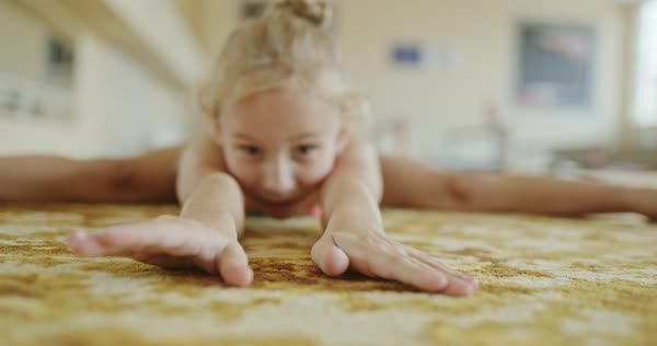 Little girl in leotard bending forward and stretching body while doing split on floor in gym - Stock Video Footage - Dissolve