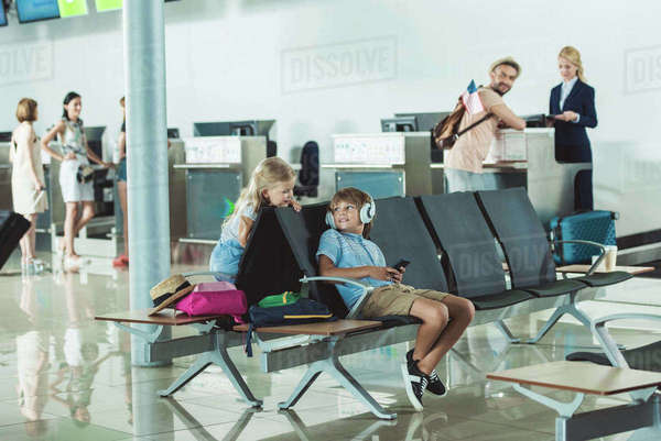 Boy In Headphones Using Smartphone With Sister Near By And Father At 