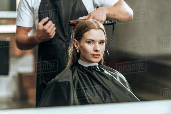 Cropped Shot Of Hairstylist Using Hair Straightener And Girl
