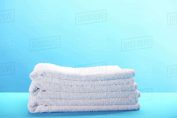Pile of clean soft white towels on blue background - Stock Photo - Dissolve