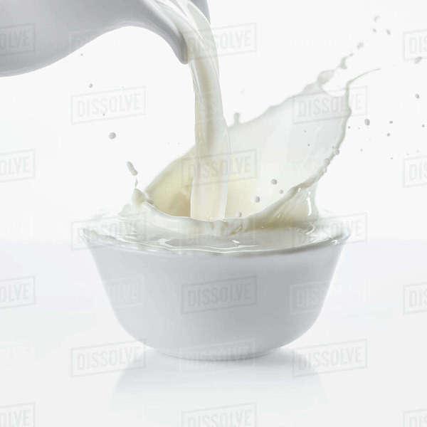 Pouring milk from jug in bowl on white background Stock Photo Dissolve