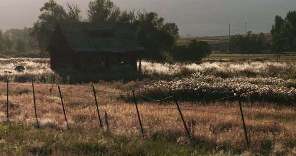 An Old Cabin Sits Behind A Fence In A Beautiful Mountain Meadow