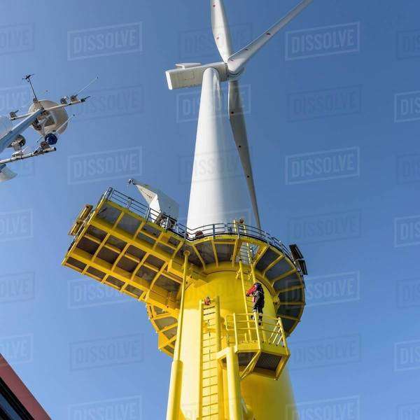 Engineer climbing wind turbine from boat at offshore windfarm, low