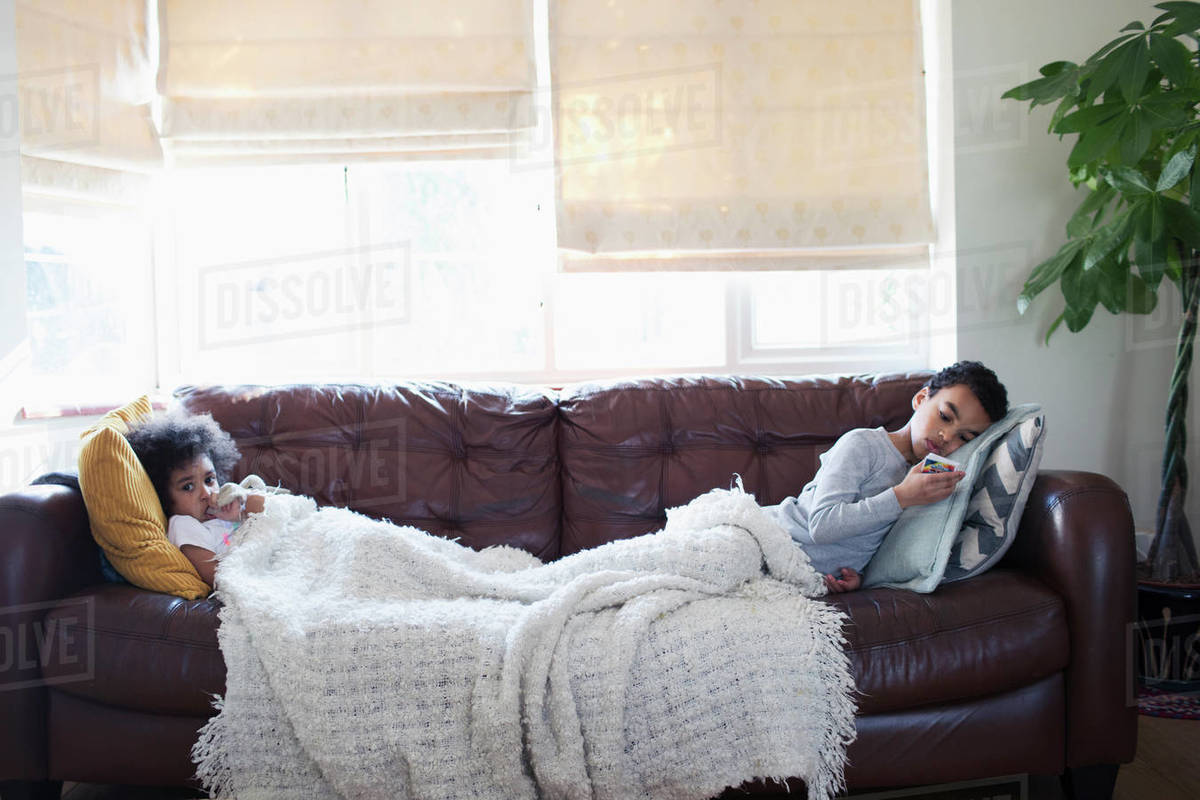 Brother And Sister Relaxing Watching Tv On Living Room Sofa Stock Photo
