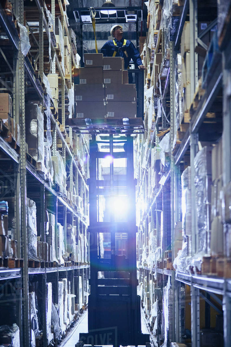 Worker operating forklift stacking cardboard boxes on distribution