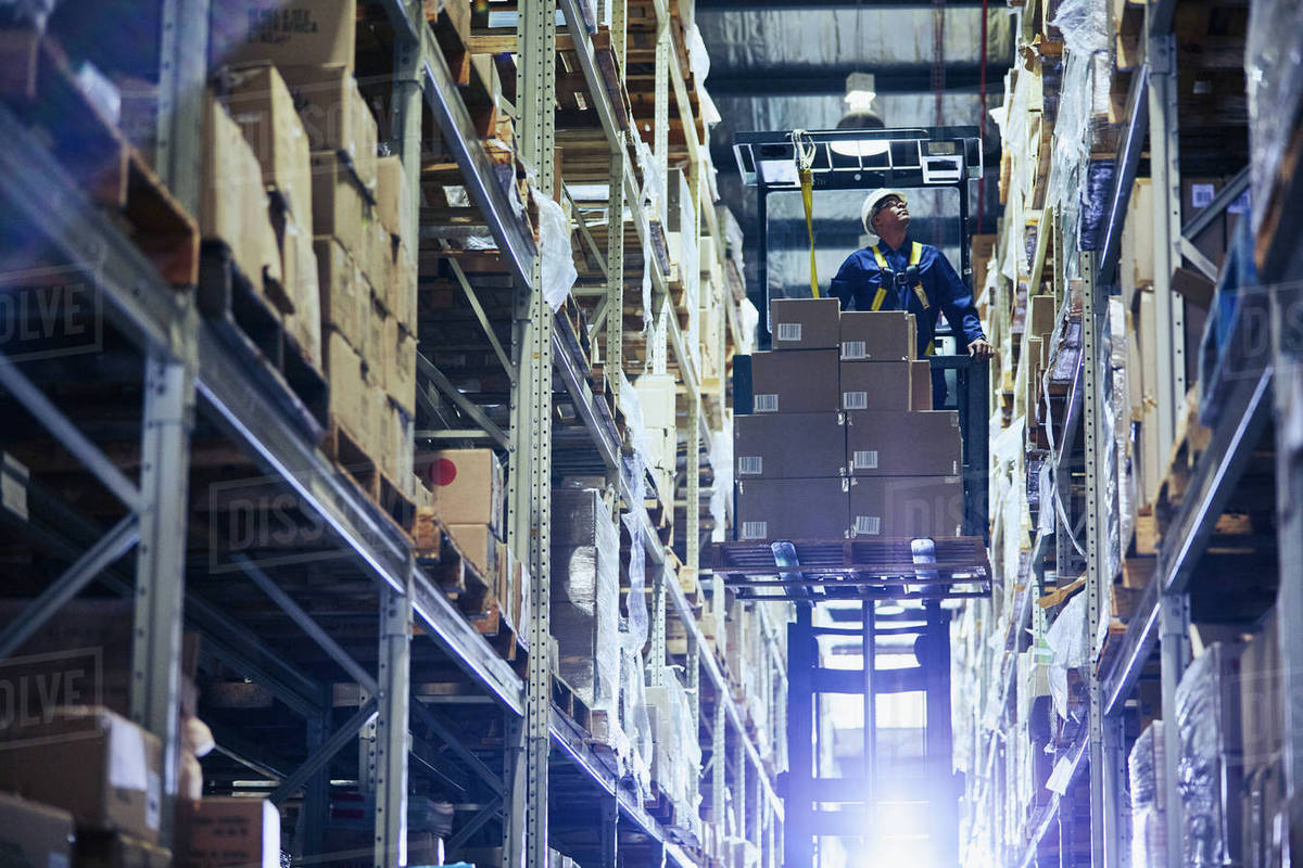 Worker operating forklift stacking cardboard boxes on distribution