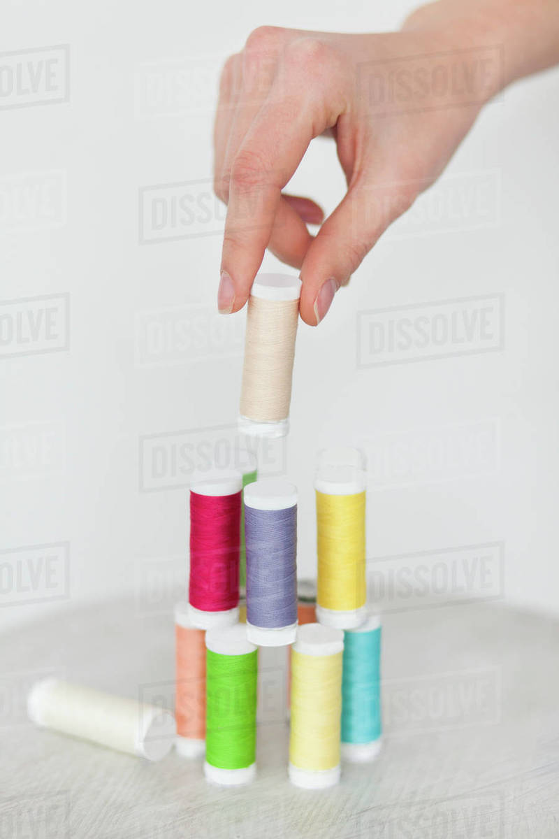 Hand of woman stacking colorful spools of thread - Stock Photo - Dissolve