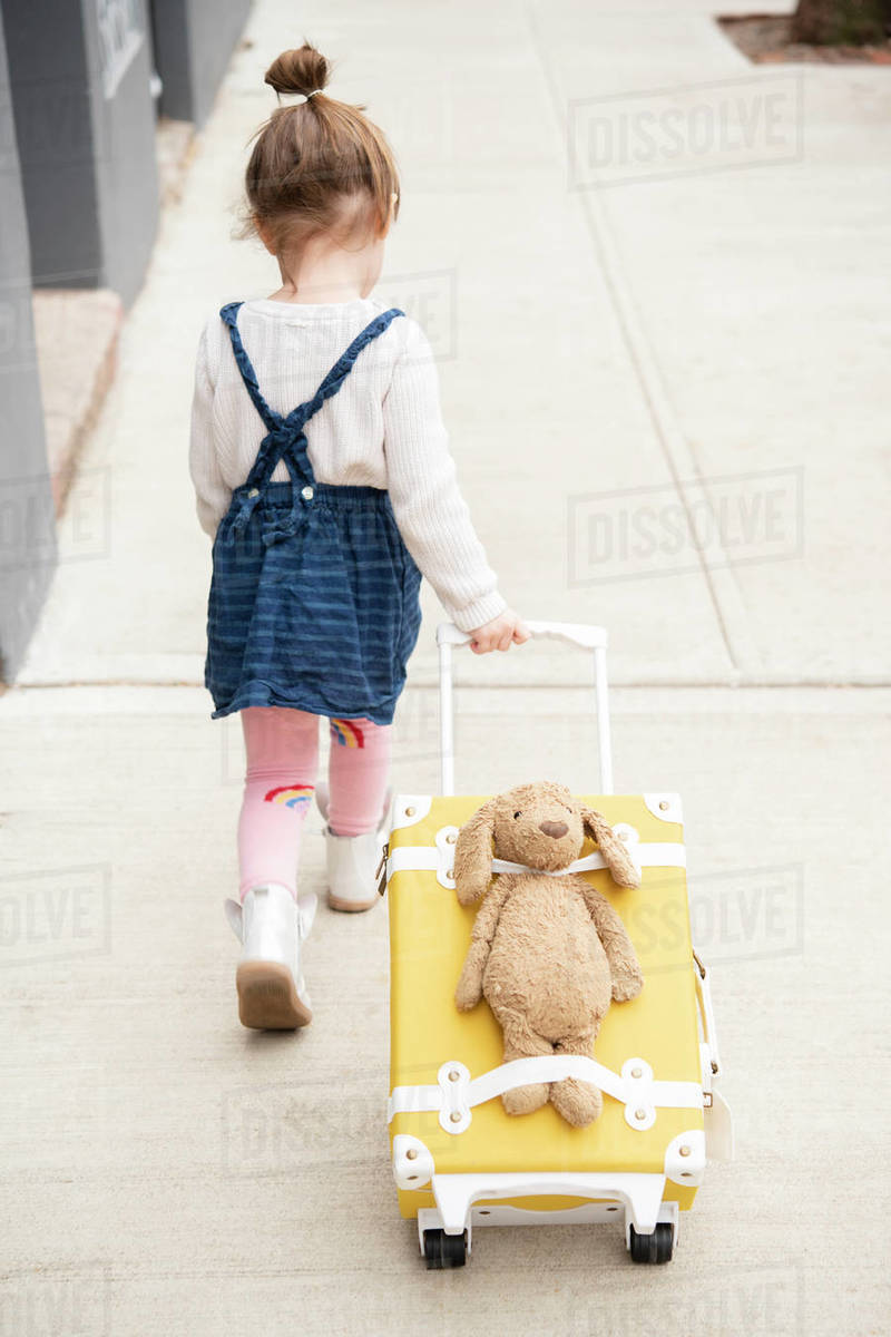 Girl pulling suitcase with teddy bear strapped to it Stock Photo