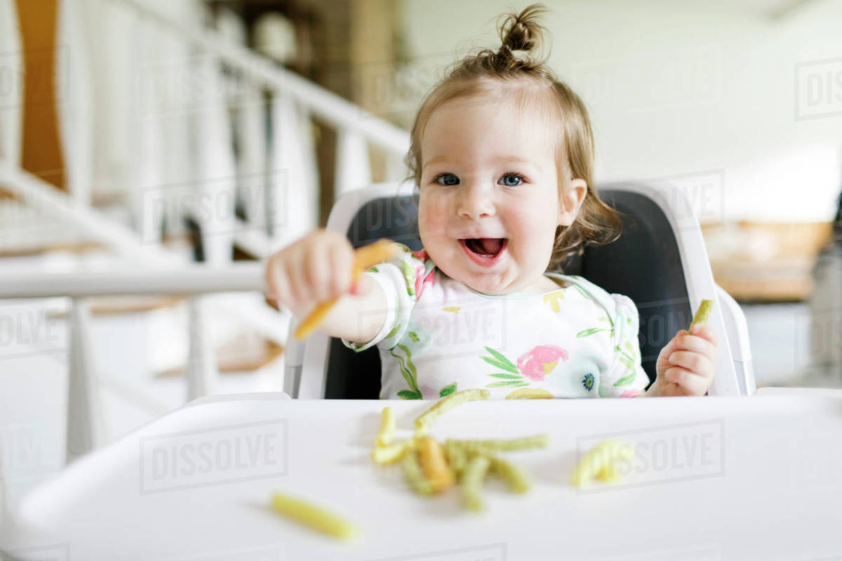 Baby girl eating in high chair Stock Photo Dissolve