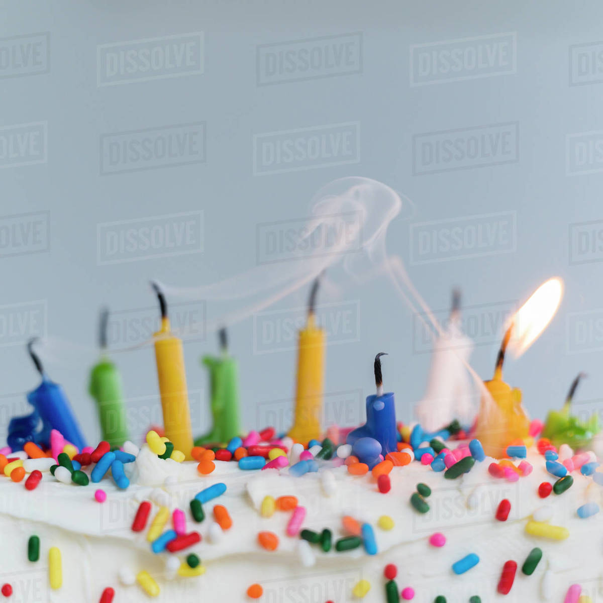 Extinguished birthday candles on cake one still burning Stock Photo