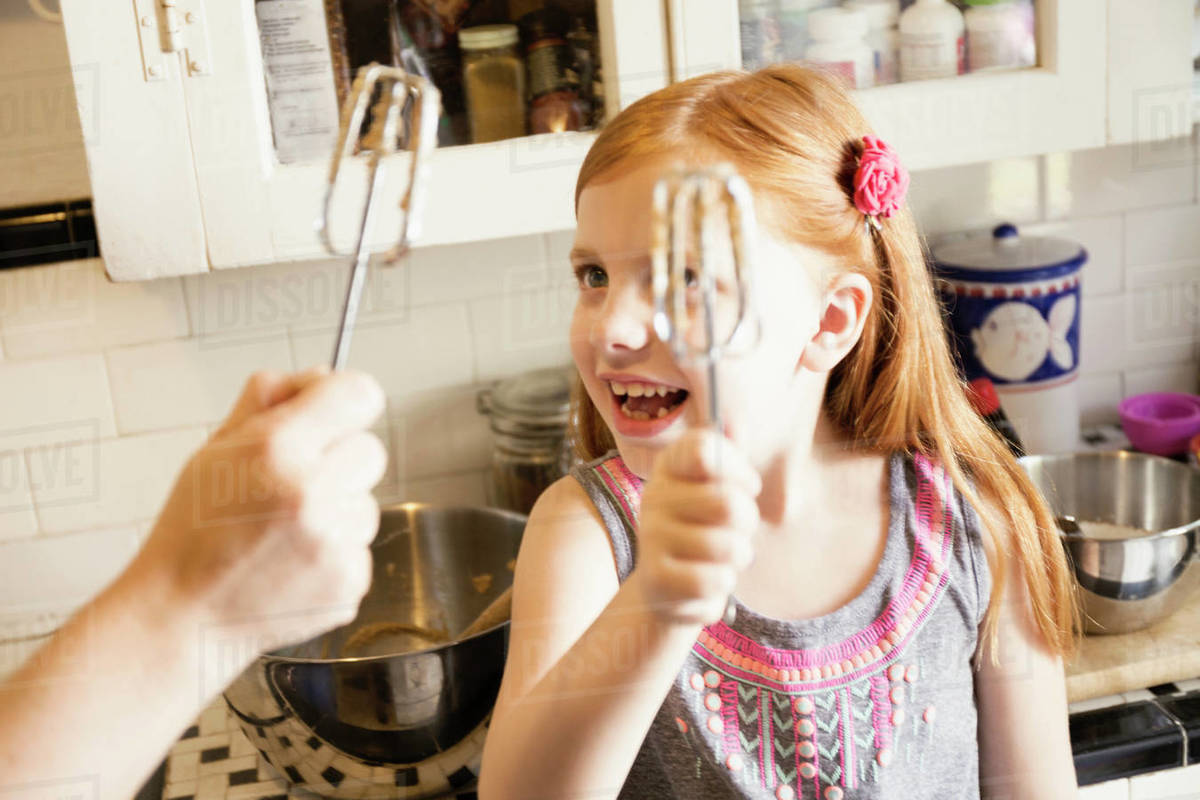 Girl and mother holding up whisks in kitchen Stock Photo Dissolve