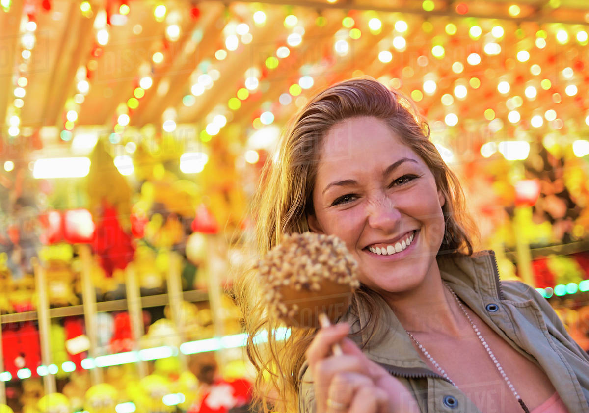 Woman holding caramel apple at funfair Stock Photo Dissolve