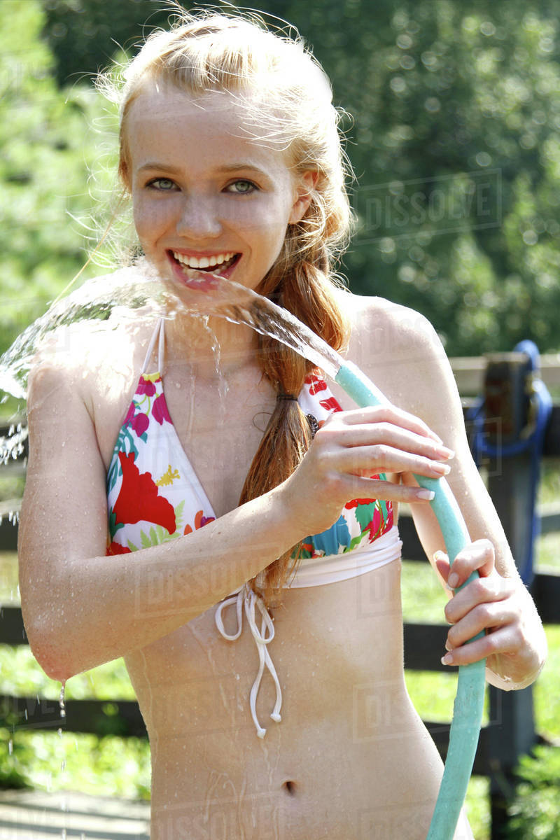 Teenage girl (14-15) wearing bikini drinking water from garden hose - Stock  Photo - Dissolve