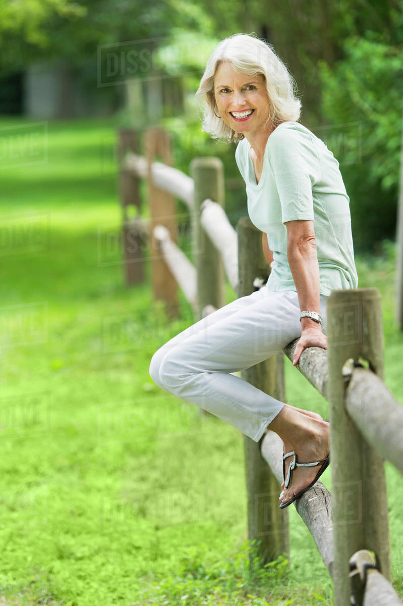 Portrait of senior woman sitting on fence - Stock Photo - Dissolve