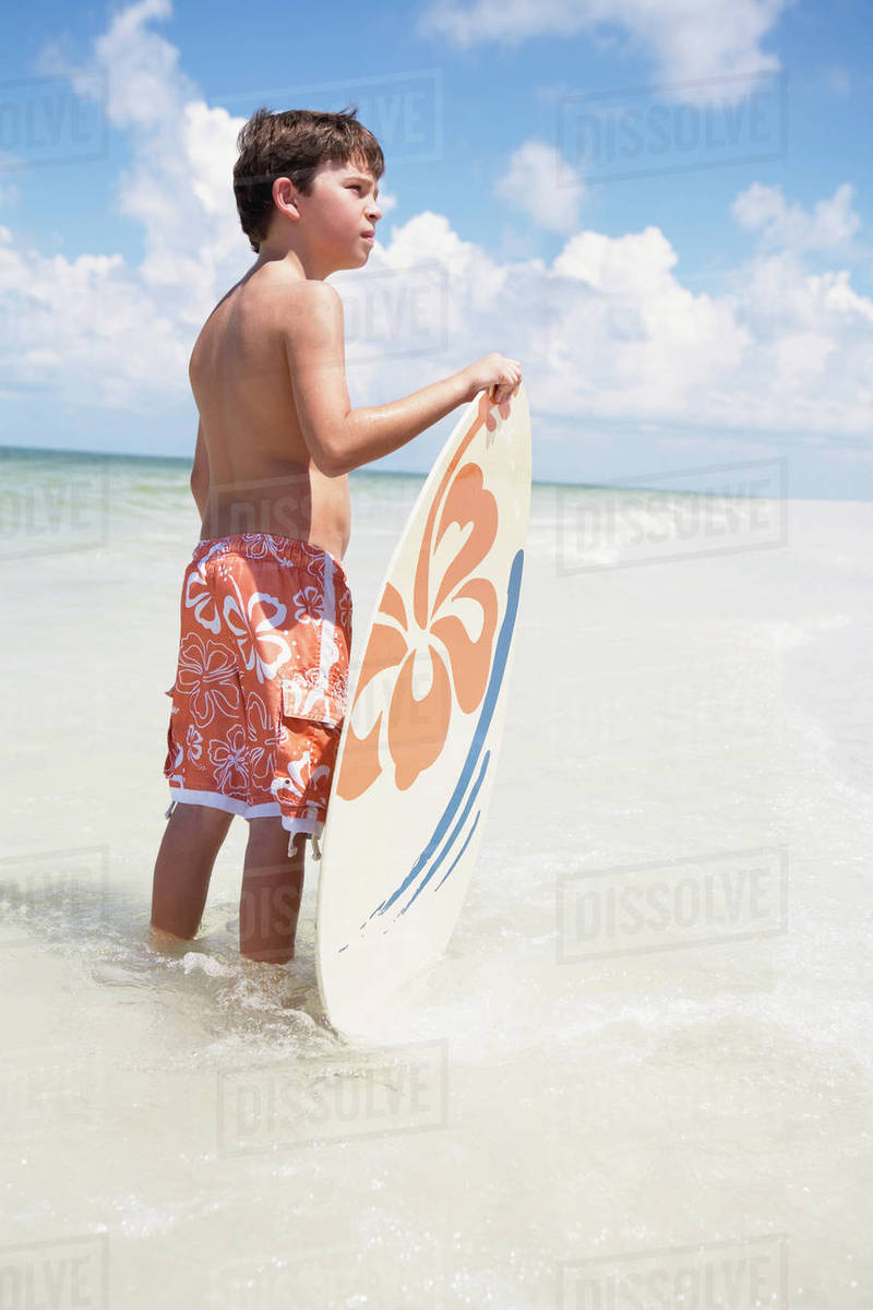 Boy holding skimboard in ocean Stock Photo Dissolve
