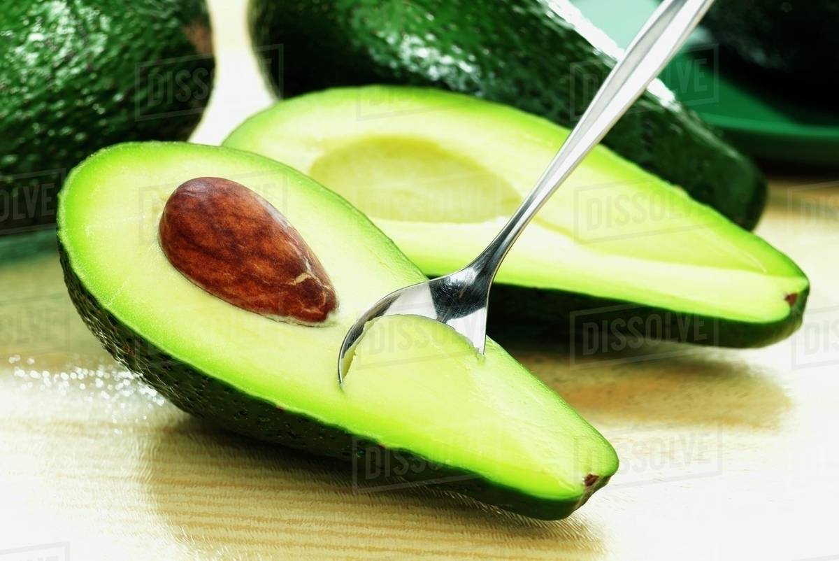 An avocado, halved, with a spoon Stock Photo Dissolve