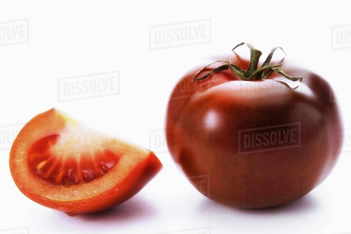 A whole tomato and a wedge of tomato, variety 'Kumato' Stock Photo