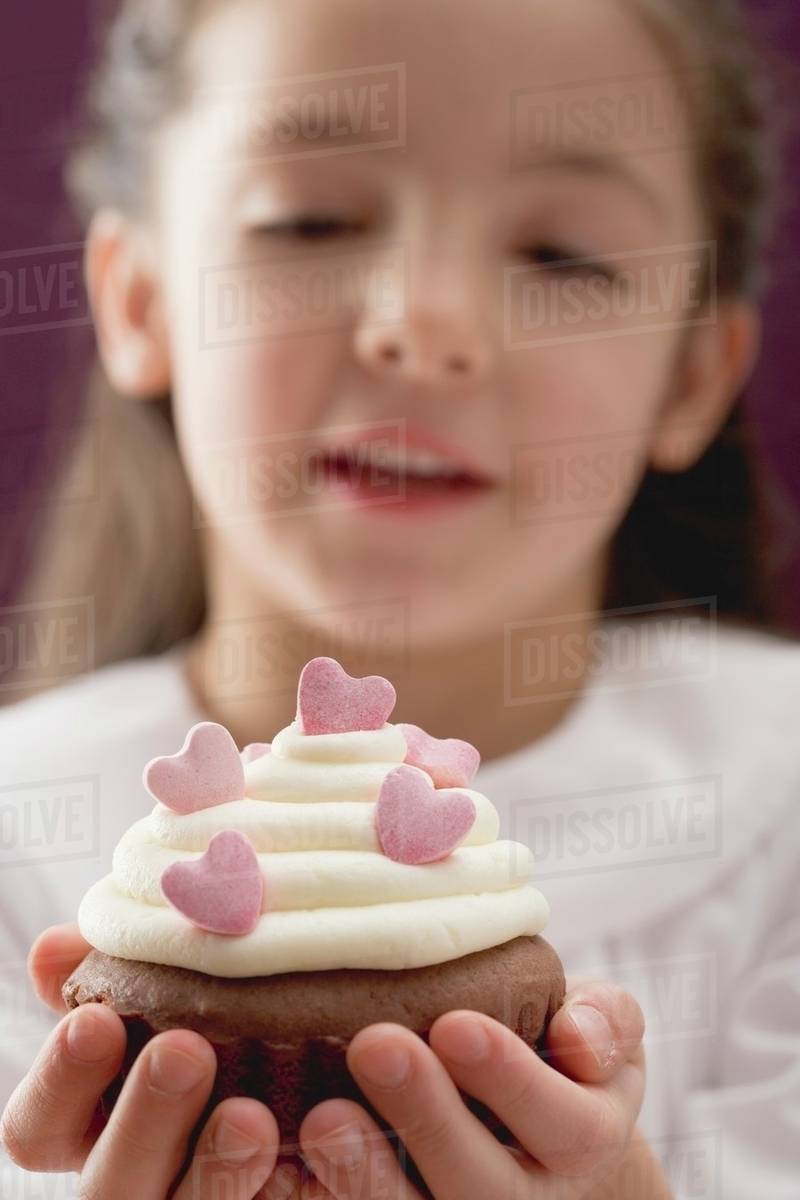 Little girl holding cupcake with sugar hearts Stock Photo Dissolve