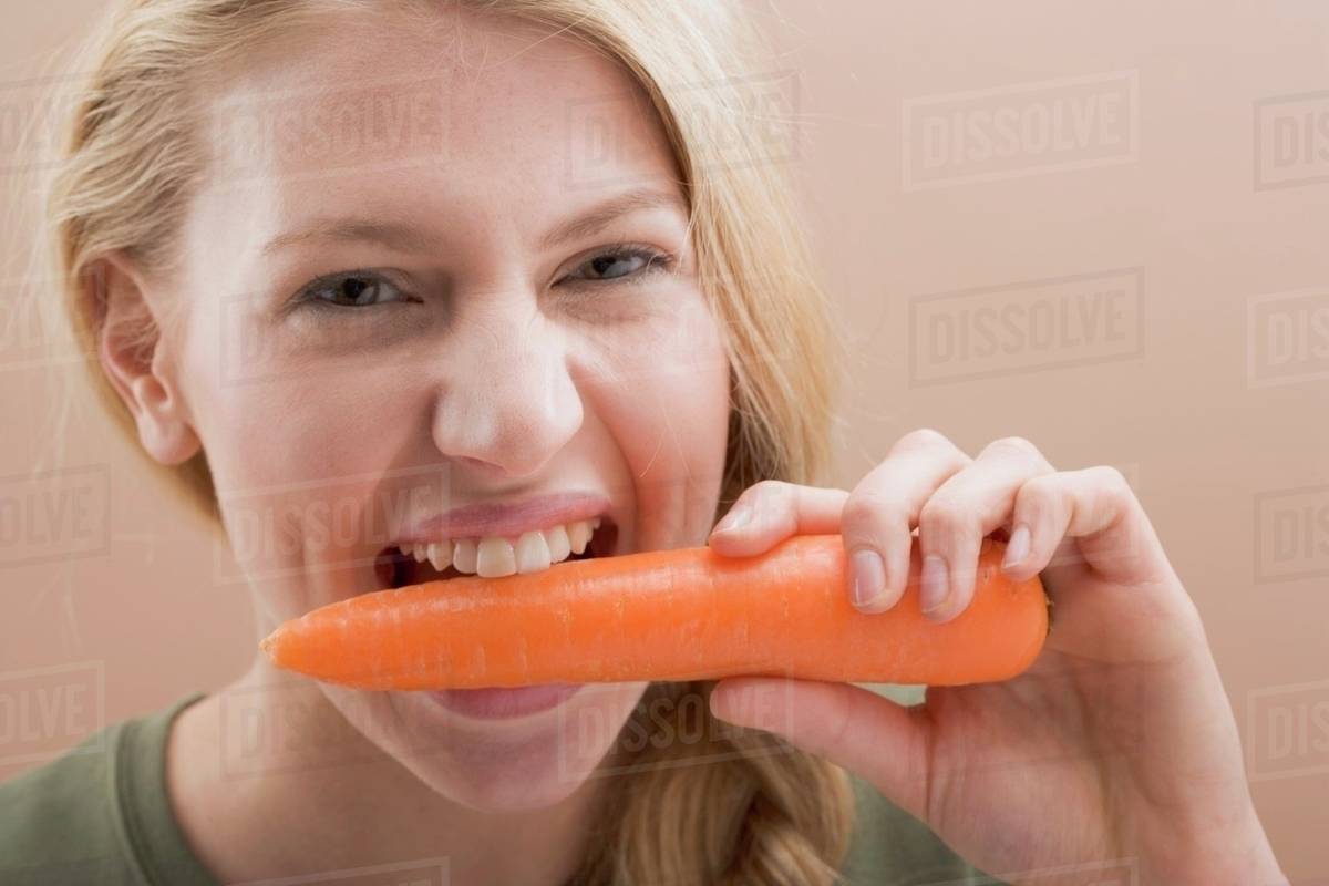 Woman biting a fresh carrot Stock Photo Dissolve