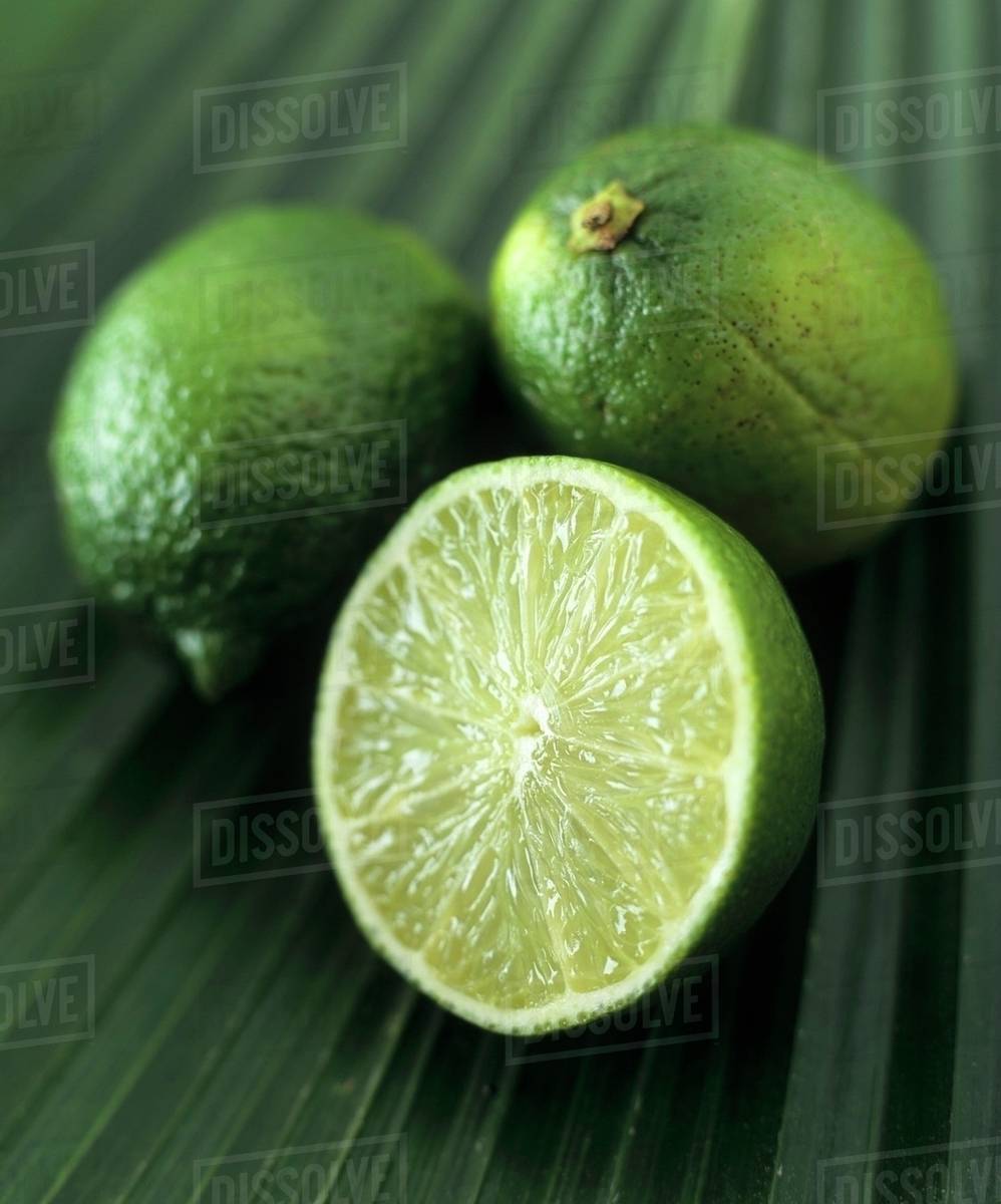 Limes, two whole and one half, on a palm leaf Stock Photo Dissolve