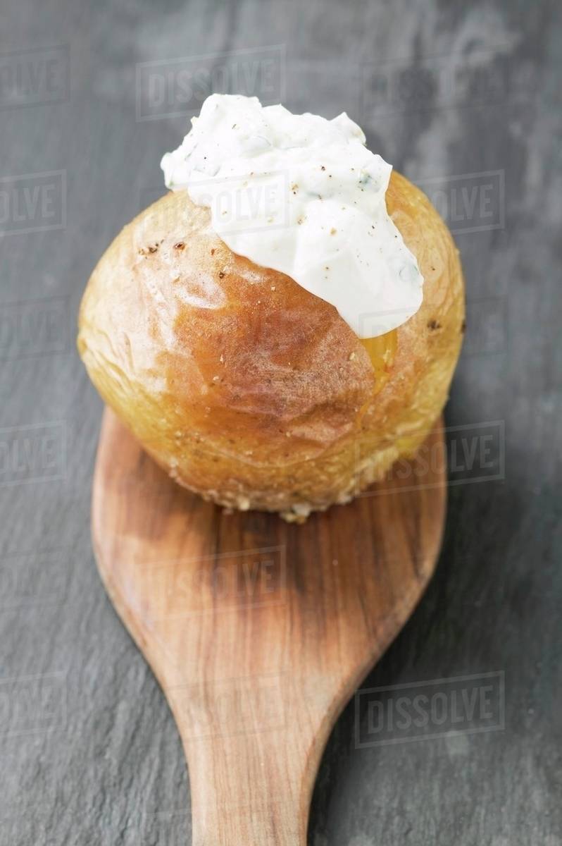 Baked potato with quark on wooden spoon Stock Photo Dissolve
