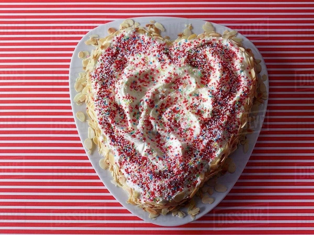 A Heart Shaped Cake Decorated With Colourful Sprinkles And Flaked