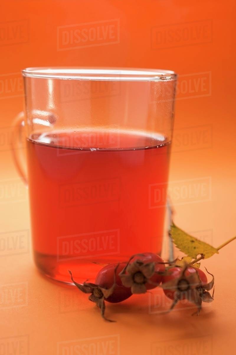 Rose hip tea in glass cup, sprig of fresh rose hips Stock Photo