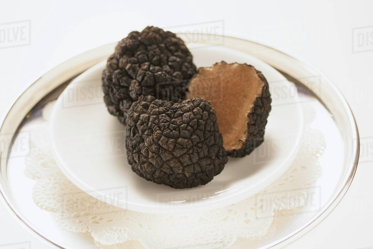 Black truffles, whole and halved, on plate Stock Photo Dissolve