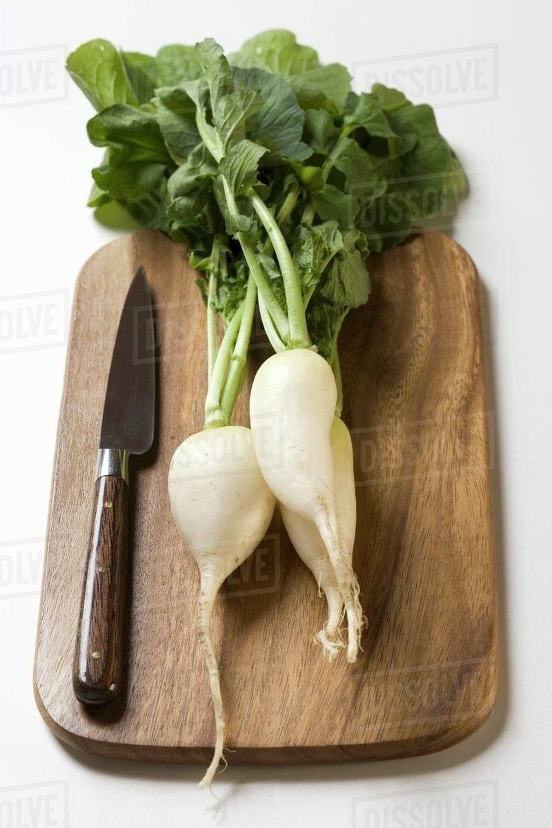icicle radishes with leaves knife on chopping board stock photo