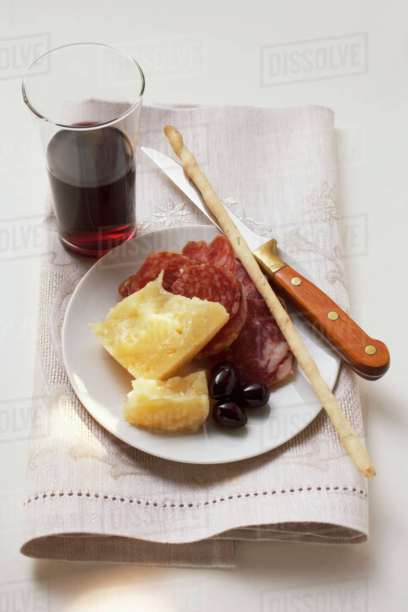 Salami, cheese, olives & grissini on plate, glass of red wine Stock
