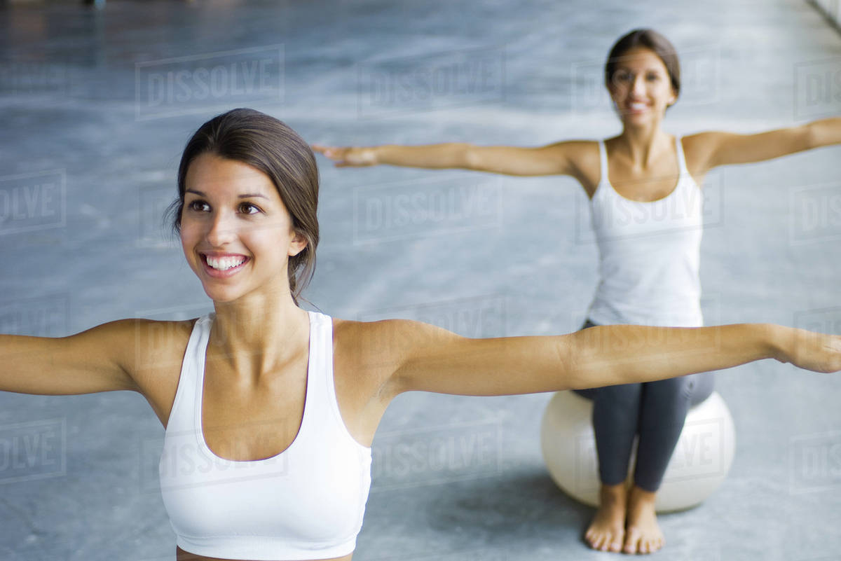 Teenage twin sisters sitting on fitness balls, arms outstretched, both smiling Royalty-free stock photo