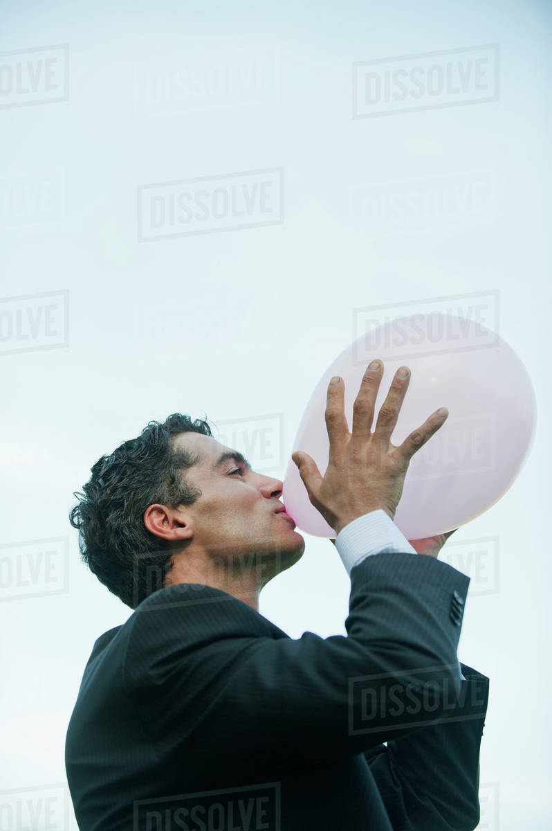 Businessman blowing up balloons Stock Photo Dissolve