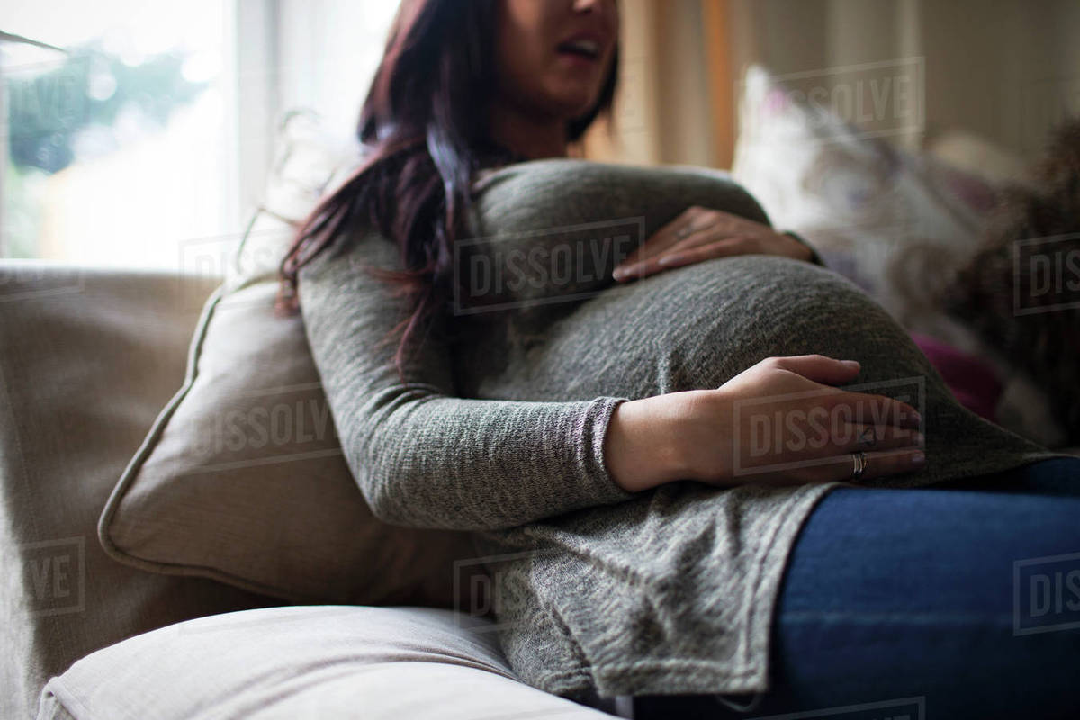 Pregnant woman on sofa holding stomach Stock Photo Dissolve