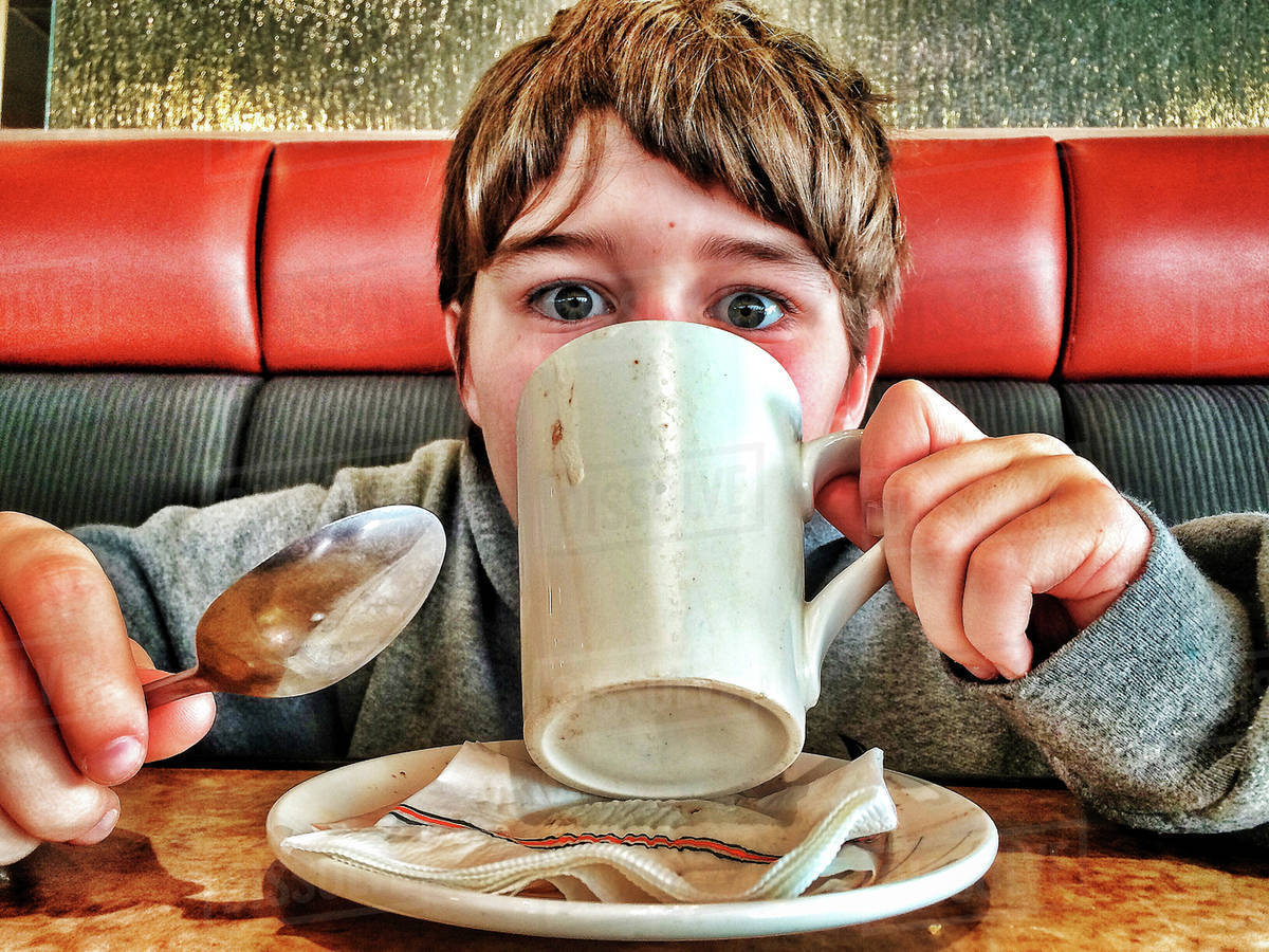 Caucasian boy drinking coffee in diner Stock Photo Dissolve