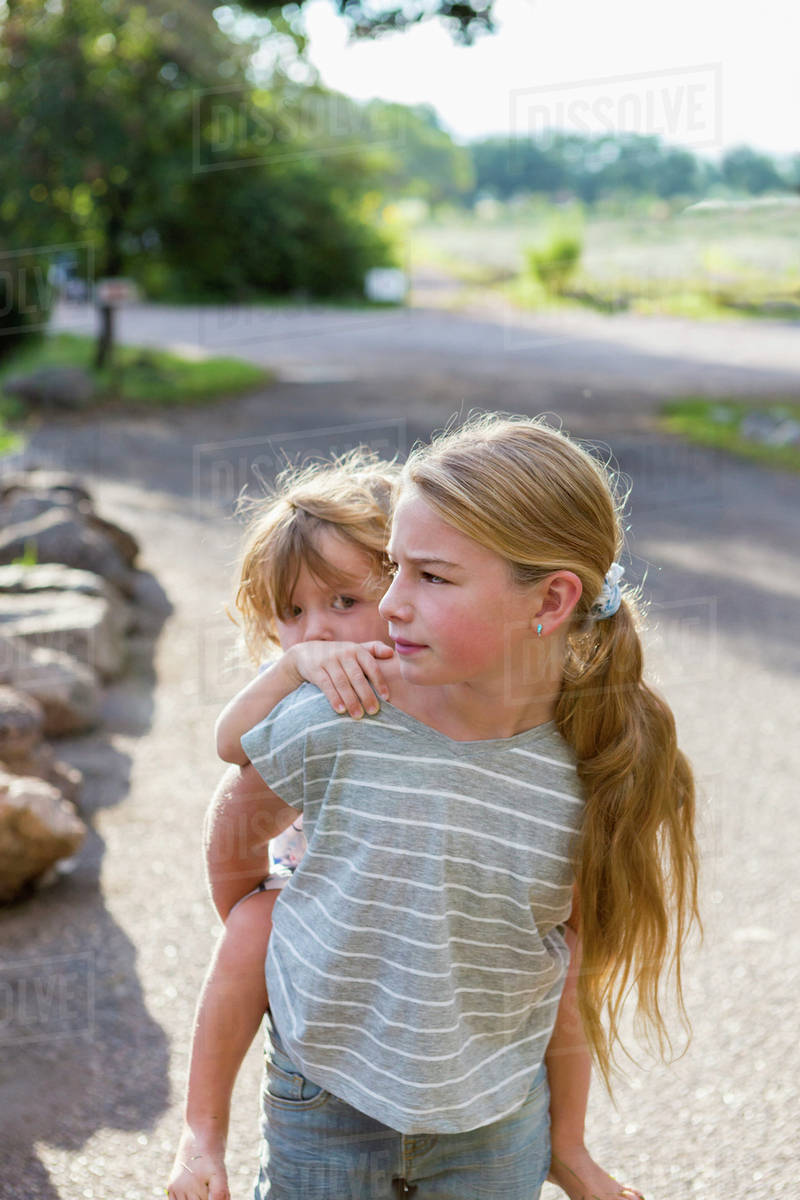Caucasian girl carrying toddler brother piggyback Stock Photo Dissolve