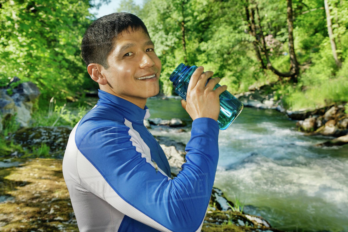 Mixed race man drinking water near river Stock Photo Dissolve