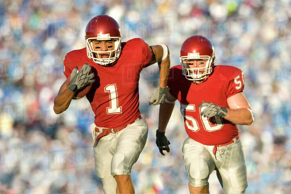 Football players running on field in game Stock Photo Dissolve