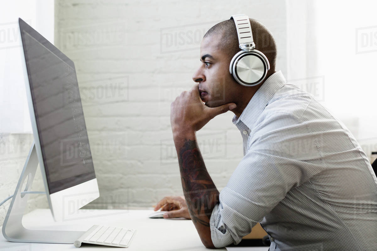 Mixed race businessman listening to headphones and working at desk