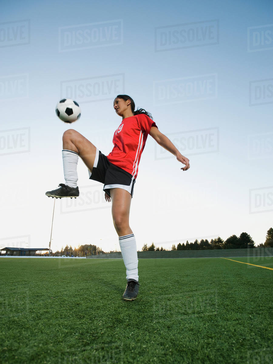 Mixed race woman bouncing soccer ball on knee Stock Photo Dissolve