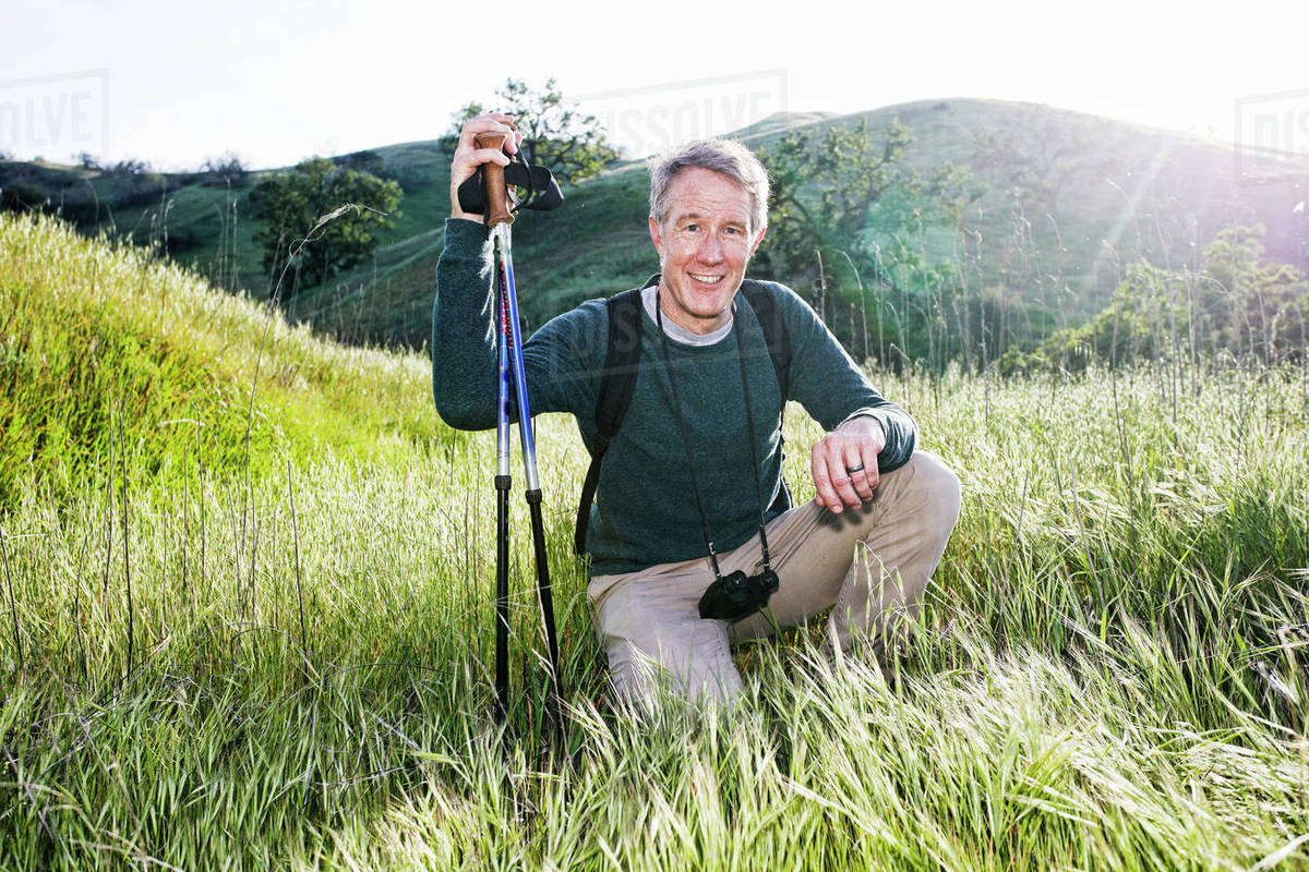 Caucasian hiker kneeling in grass on mountain Stock Photo Dissolve