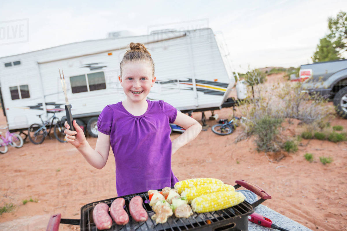Caucasian girl cooking on grille while camping Stock Photo Dissolve