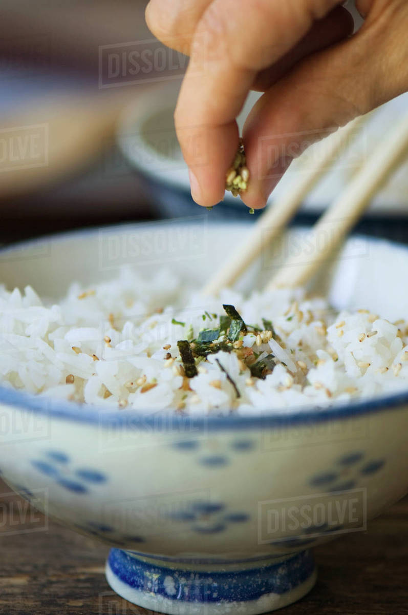 Hand putting seasoning on bowl of rice with chopsticks Stock Photo