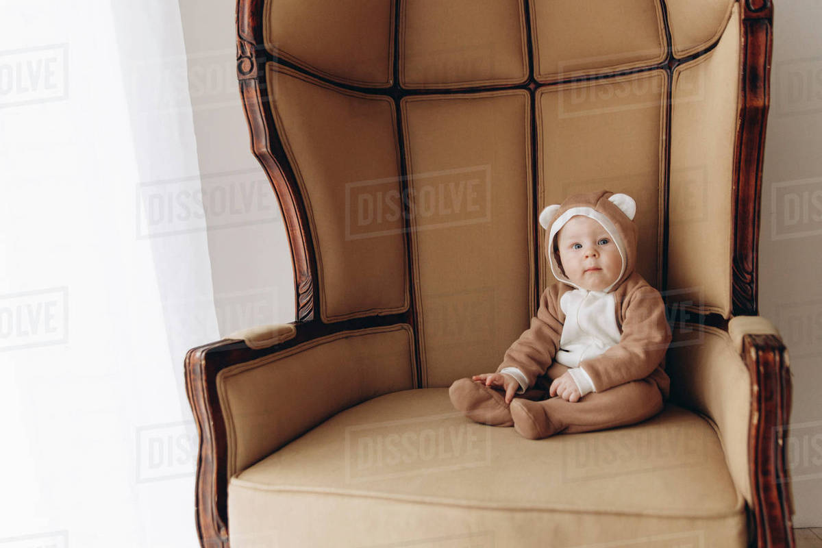 Caucasian baby boy sitting in armchair wearing bear costume Stock