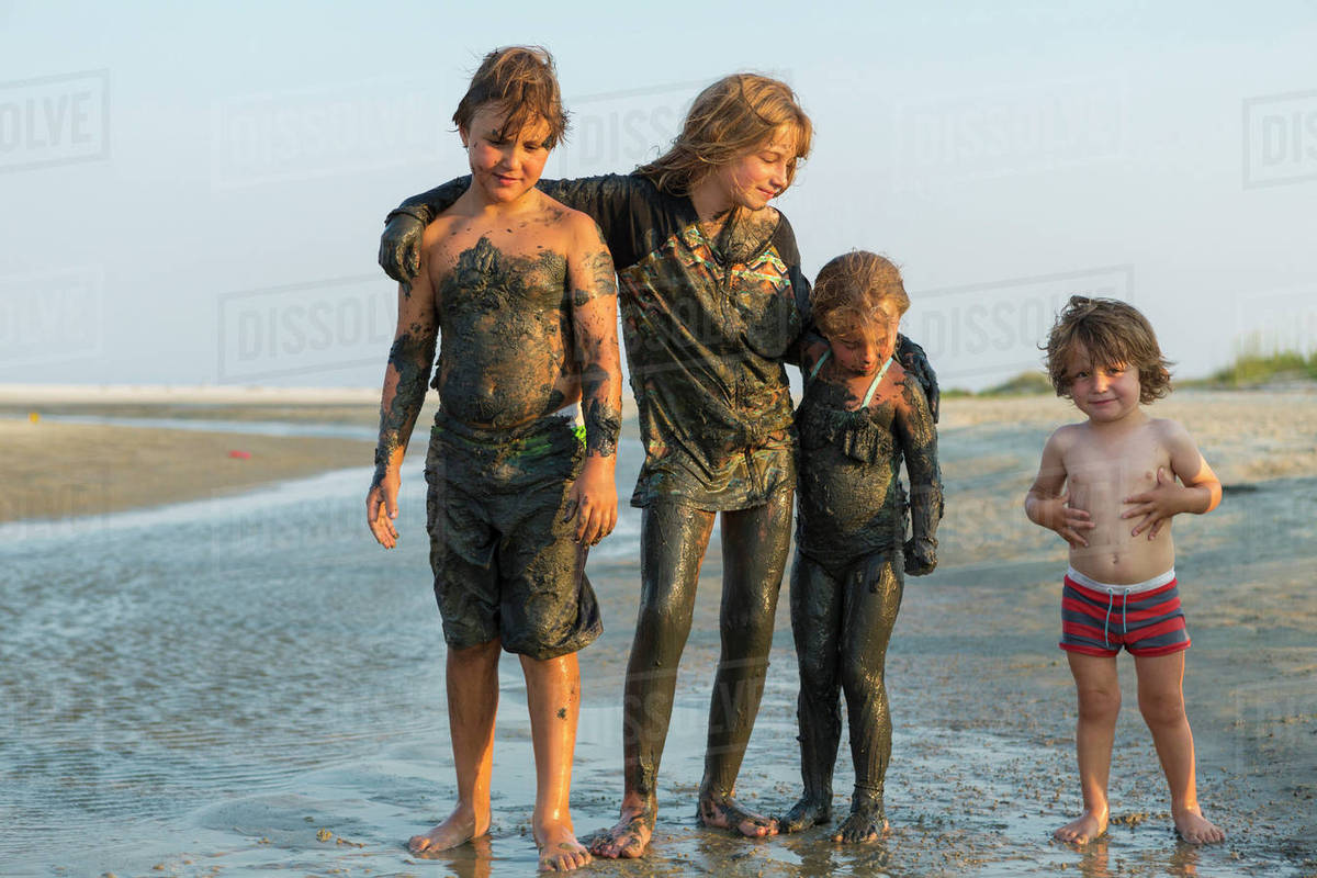 Caucasian brothers and sisters covered in mud standing on beach