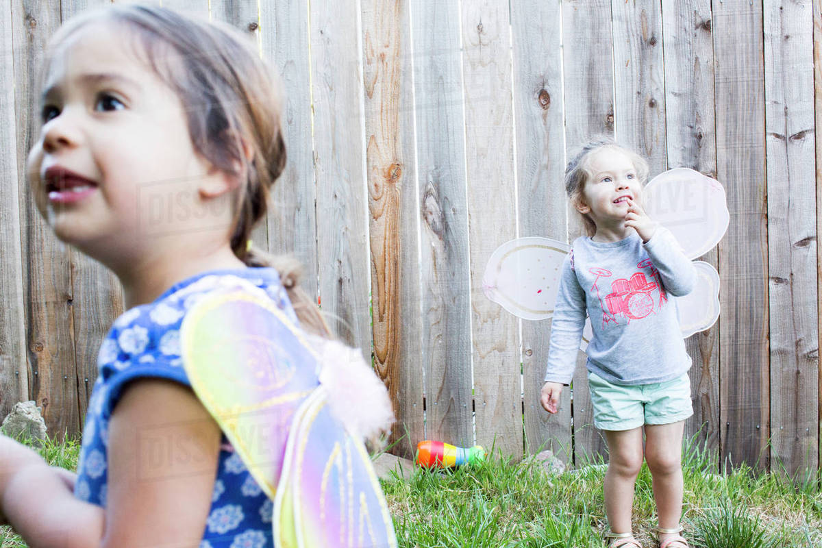 Curious girls wearing fairy wings in backyard Royalty-free stock photo