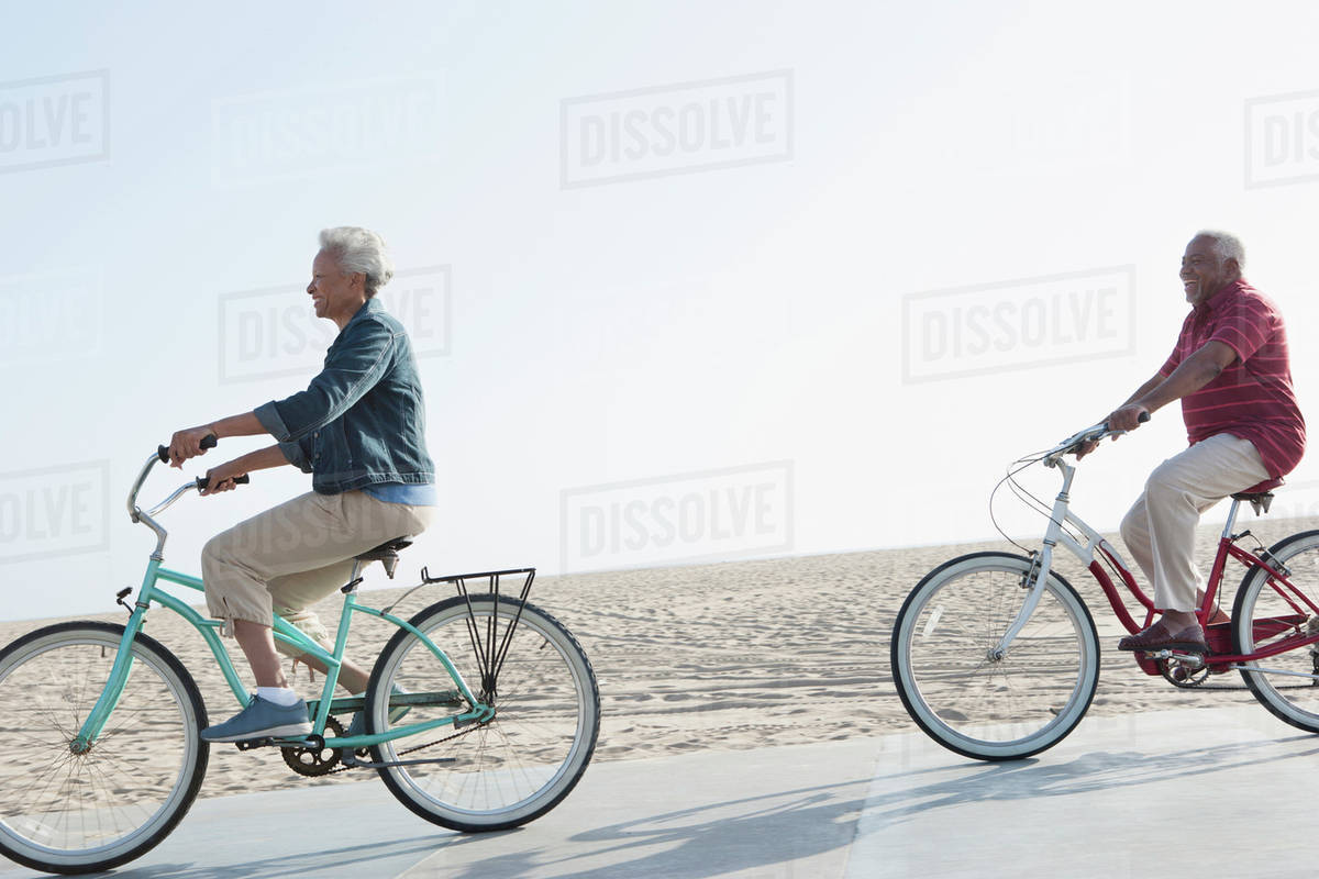 Senior African American Couple Riding Bicycles By Beach Senior African American Couple Riding Bicycles By Beach