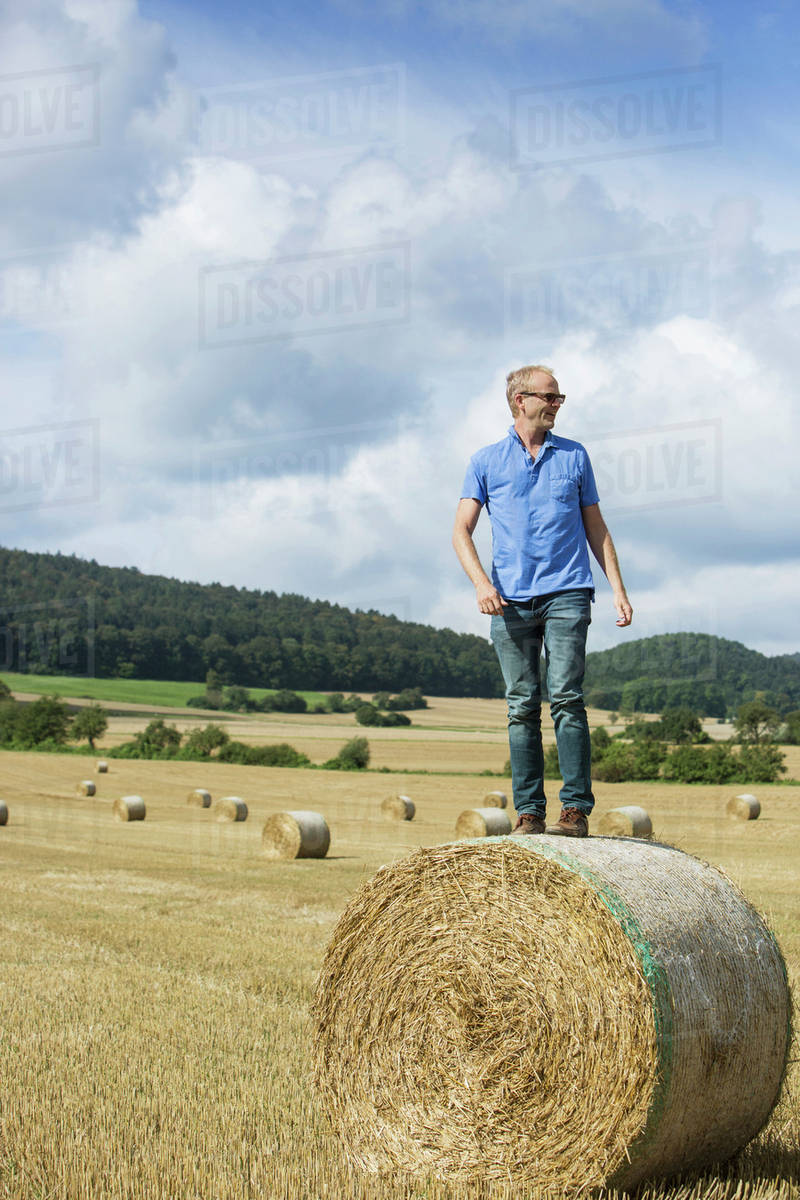 Farmer standing on hay bale in field Stock Photo Dissolve