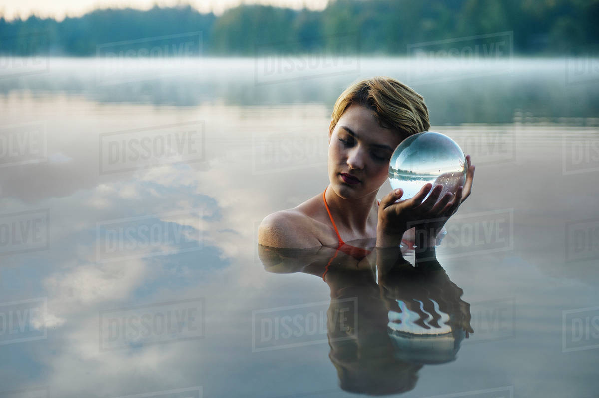 Caucasian woman holding crystal ball in still lake Stock Photo Dissolve